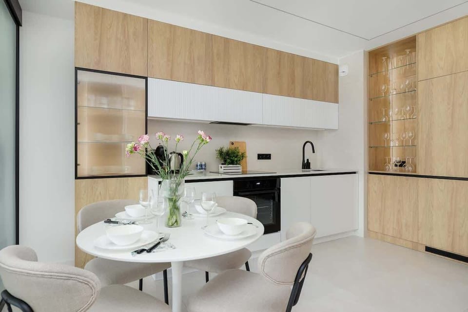 A dining area with a round table, fresh flowers, and wooden kitchen backdrop. Bright and welcoming for meals.