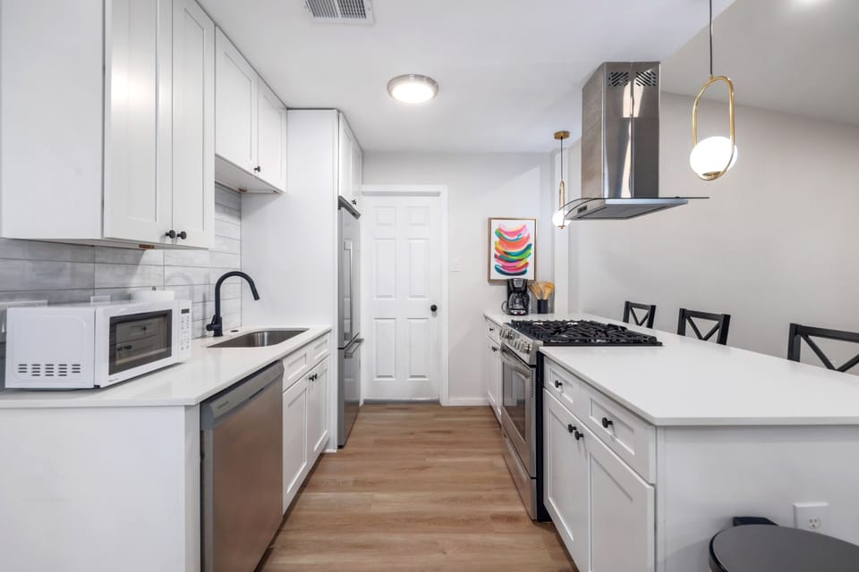This clean and modern kitchen is equipped with all the essentials, including a refrigerator, microwave, kitchen sink, dishwasher, oven, and stove. With plenty of cabinets for storage, it's perfect for preparing meals and keeping your space organized.