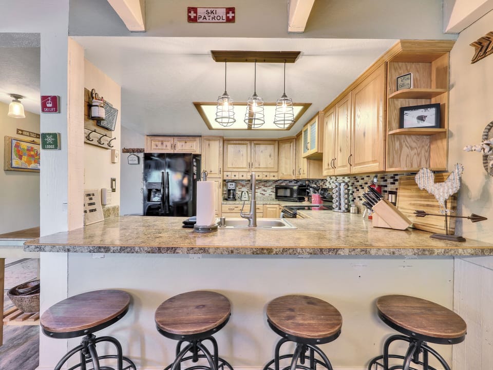 Kitchen Counter area with seating for 4, stainless steel sink, over head lighting, refrigerator, cabinetry