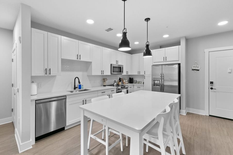 A contemporary kitchen with a clean and airy feel. The dominant color is white, which is used for the cabinets, countertops, and kitchen island, giving the space a bright and spacious look.
