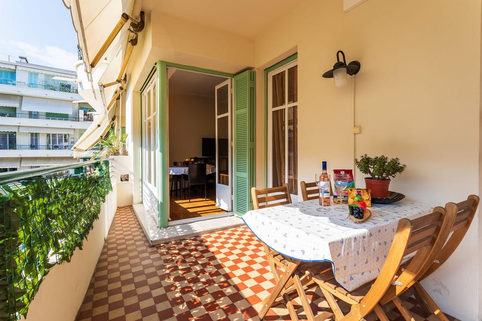 Bright terrace with decorated table, wooden chairs, plants, modern building views, and a cozy interior visible. Perfect for relaxing