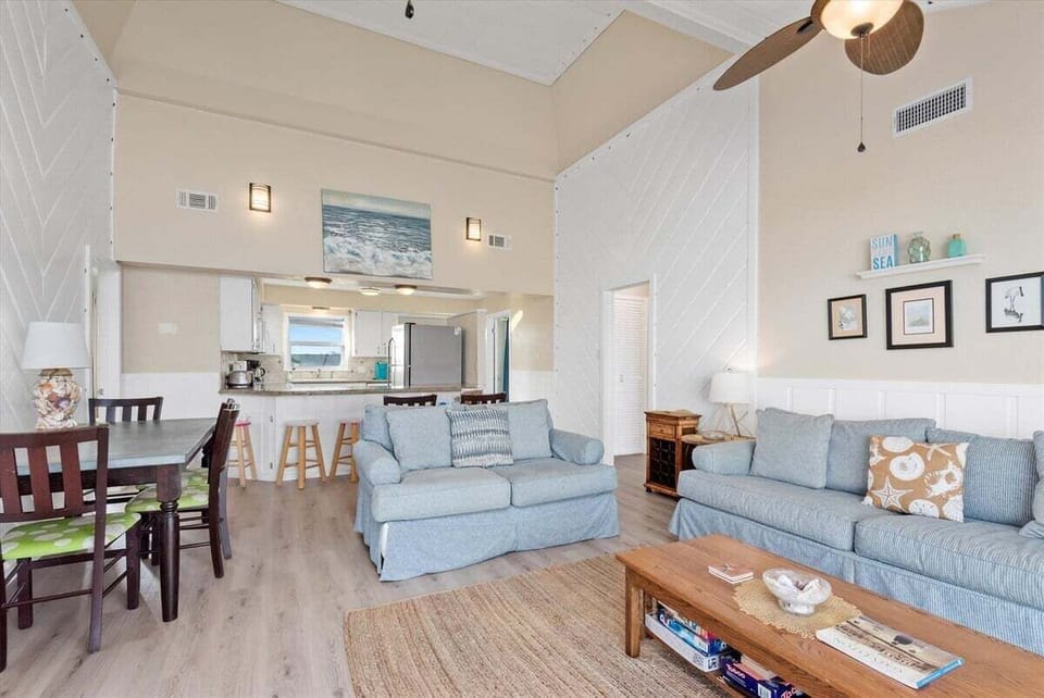 Open living and kitchen space with coastal furnishings, breakfast bar seating, and natural light near Galveston beachfront.