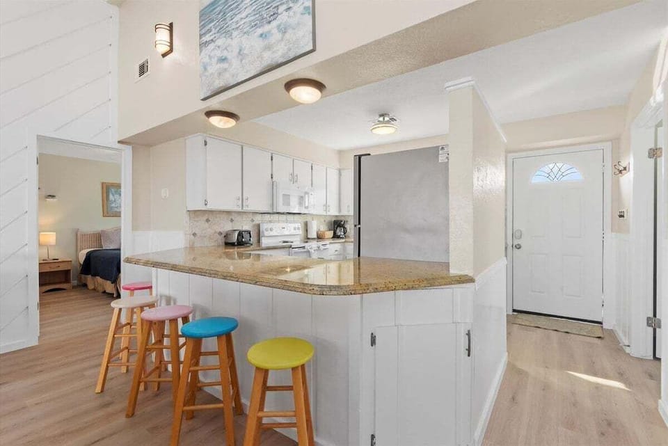 Coastal kitchen with breakfast bar, colorful stools, granite countertops, and open layout ideal for family beach vacations in Galveston.