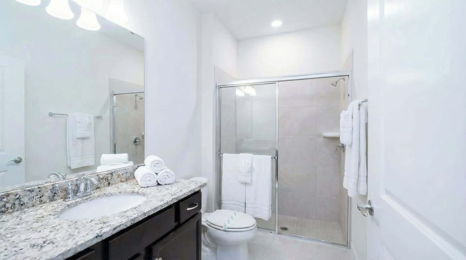 Modern bathroom with granite vanity, glass walk-in shower, and bright lighting.