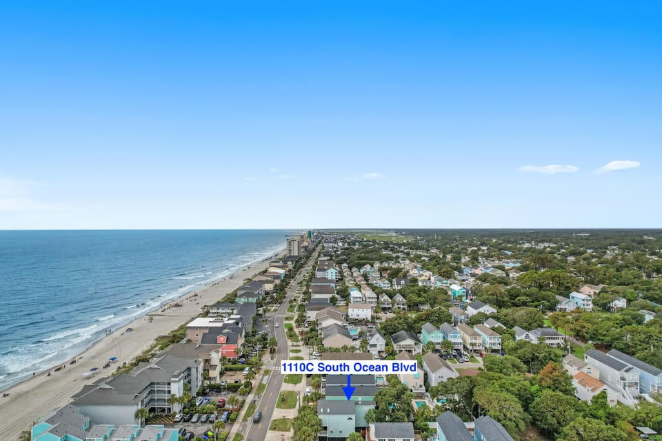 Aerial view of a community with tree-lined streets just steps from the sandy shore and sparkling ocean.