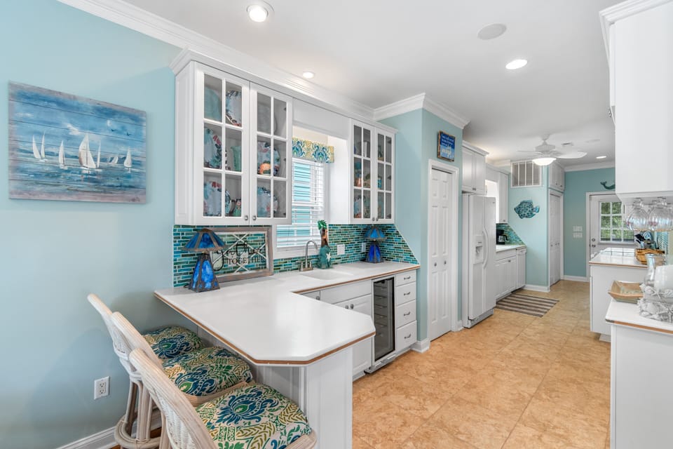Your coastal-inspired kitchen awaits with turquoise tile backsplash, white cabinetry, and charming breakfast bar seating.