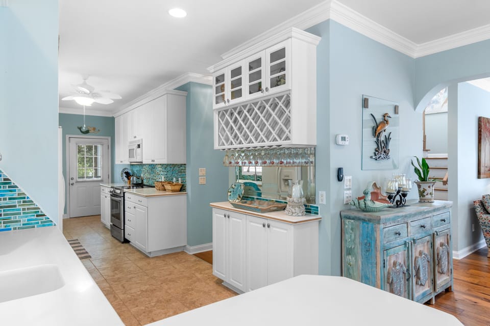 Your coastal-inspired kitchen invites culinary creativity with crisp white cabinets, ocean-blue walls, and charming turquoise backsplash that sparkles like sea glass.