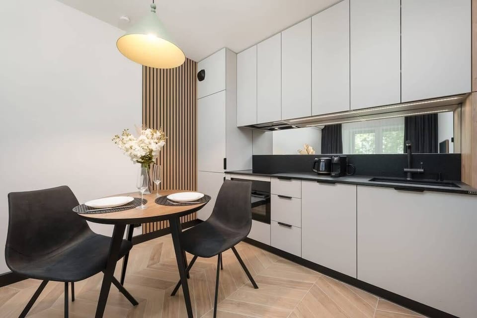 A bright dining and kitchen corner with elegant black chairs and white cabinetry. Flowers add a touch of charm to the setup.