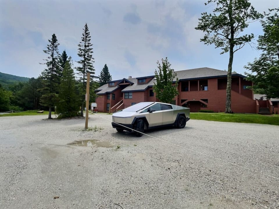 An outside view of the house with a spacious gravel parking lot in front of it.