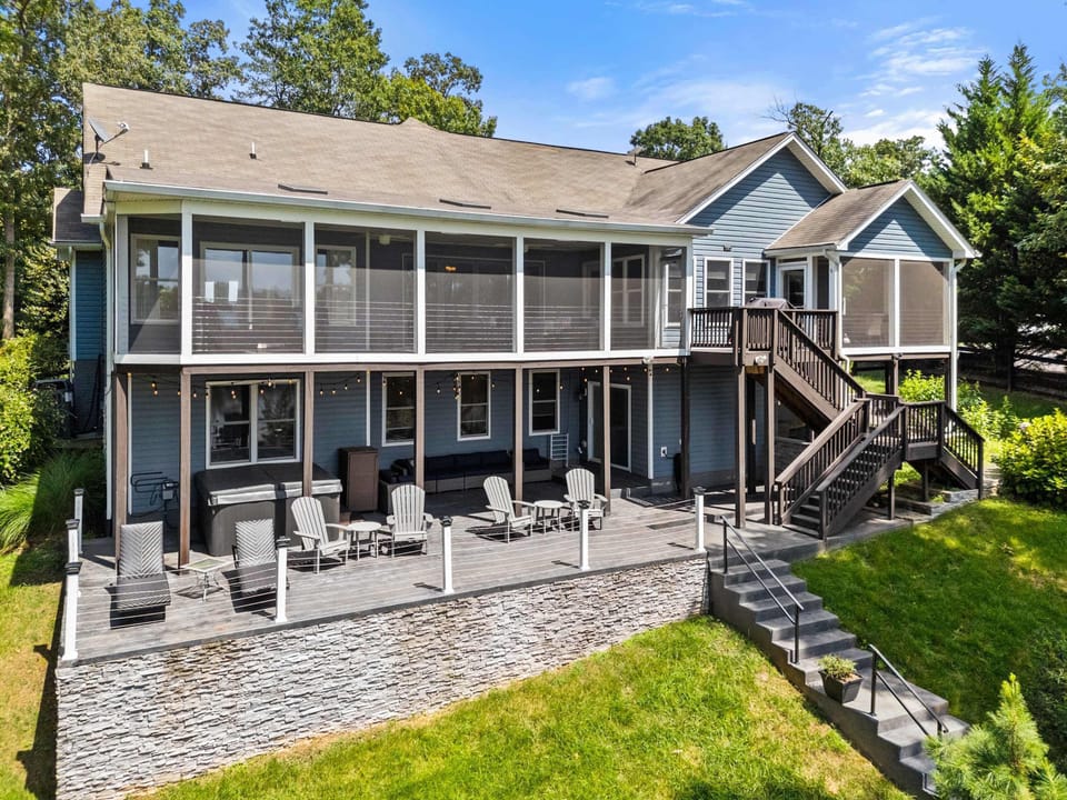 A stunning lakefront home with a spacious screened porch, surrounded by a lush green lawn and a charming stone pathway leading down to the water.