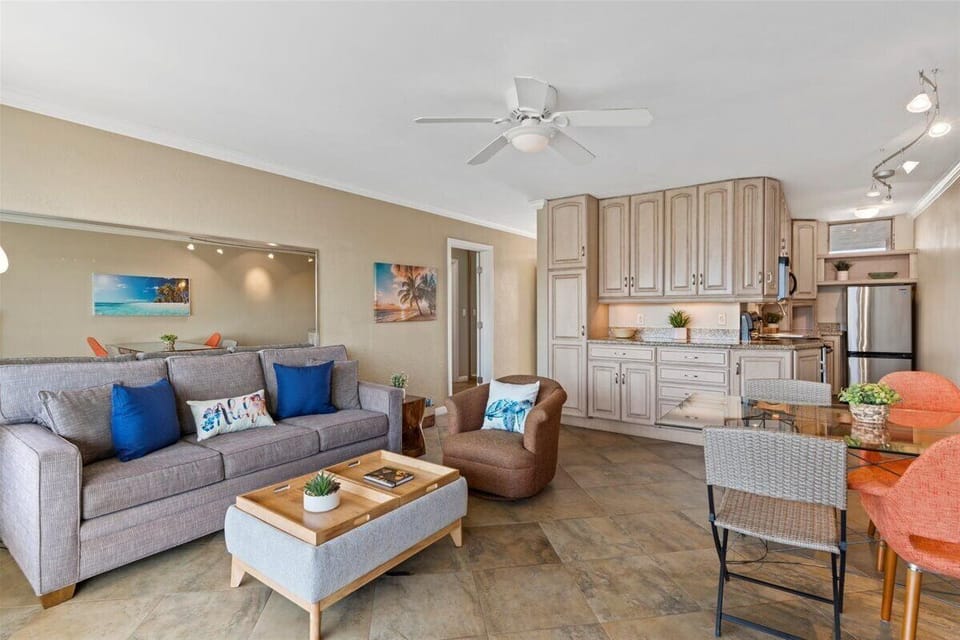 Step into your welcoming open-concept living space where coastal-inspired decor and comfortable furnishings create the perfect retreat. Relax on the sofa, enjoy your fully-equipped kitchen, and dine together at the nearby table—all under the gentle breeze 