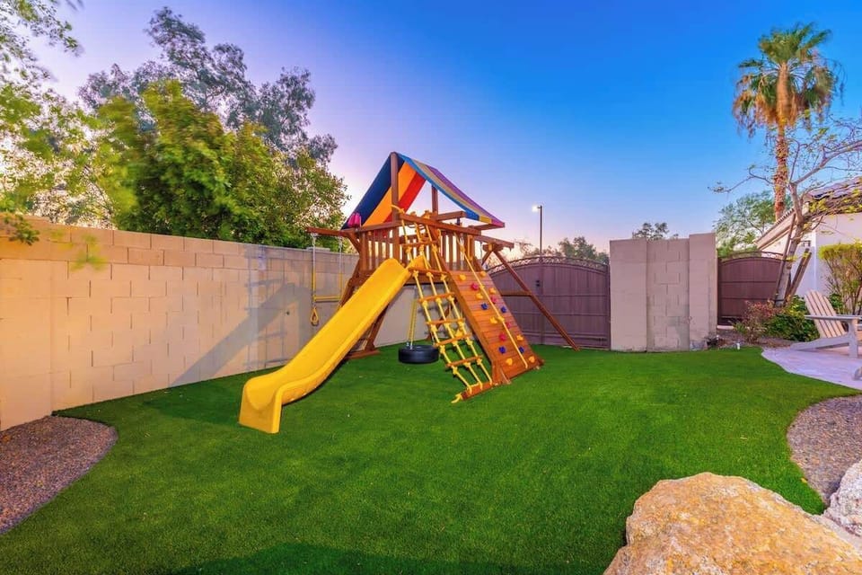 Your kids will love this private play area, complete with a colorful playset featuring a slide, climbing wall, swings, and a shaded fort on lush green turf.