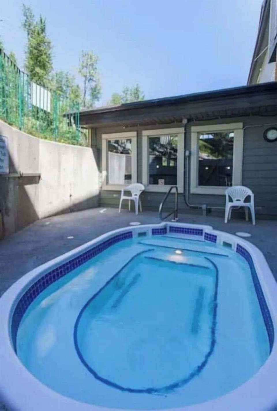 Sunny outdoor hot tub area with an oval-shaped pool, blue tile accents, and a metal handrail. 