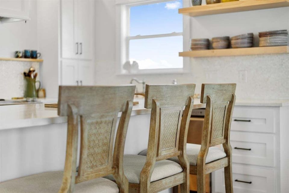 Kitchen island seating with high-back stools, white cabinetry, open shelving, and a bright coastal kitchen design.