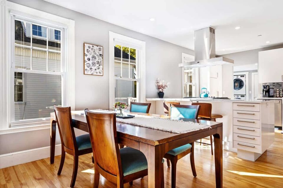 Sunlit dining area with seating for six (4 at the dining table with 2 at the bar), set beside large windows and open to the modern kitchen.