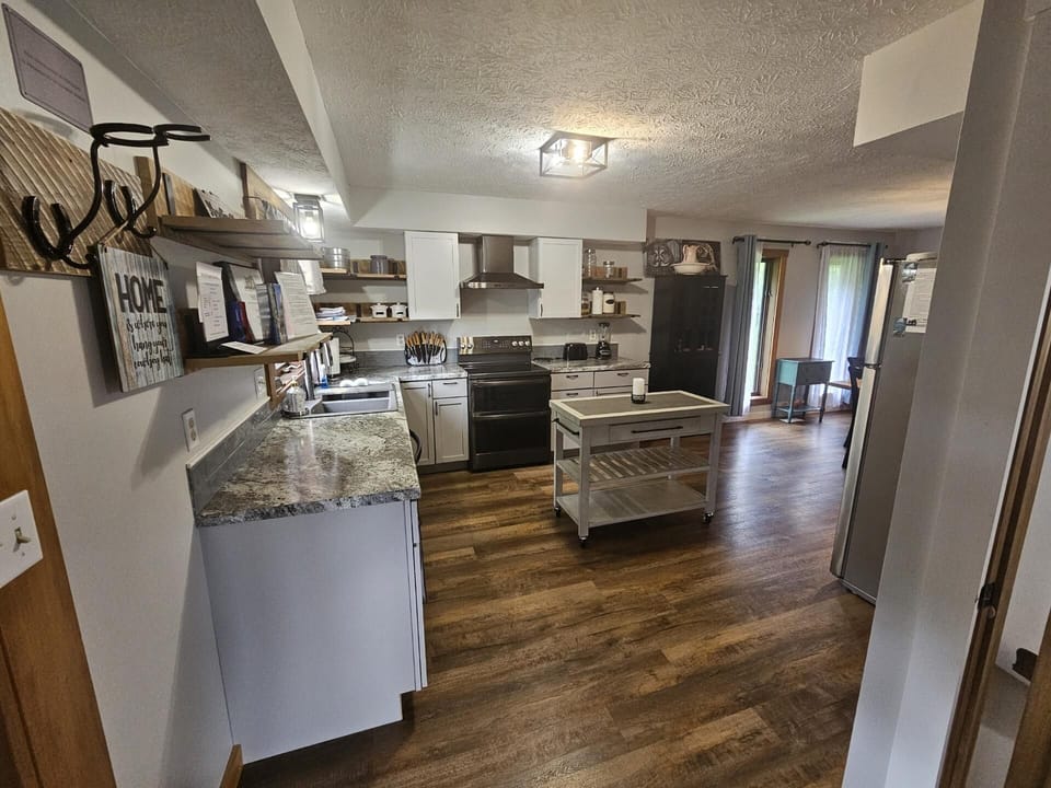 White cabinets and granite countertops surround a black stove in the kitchen with wood plank floors and a rolling island cart.