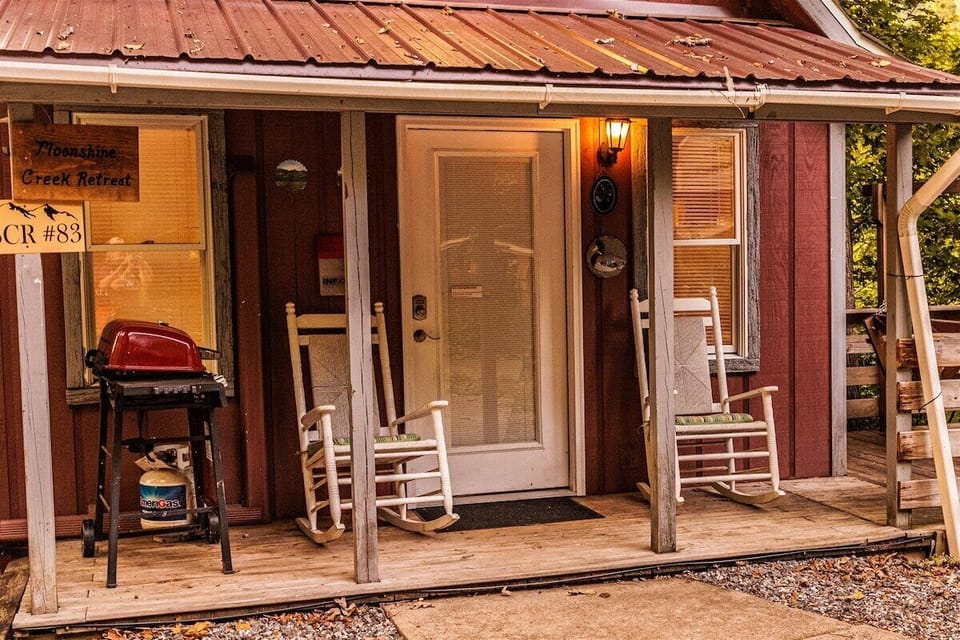 Covered front porch with rocking chairs, entry door, outdoor lighting, and grill beside the cabin. Convenient outdoor space for relaxing after exploring Bryson City attractions.
