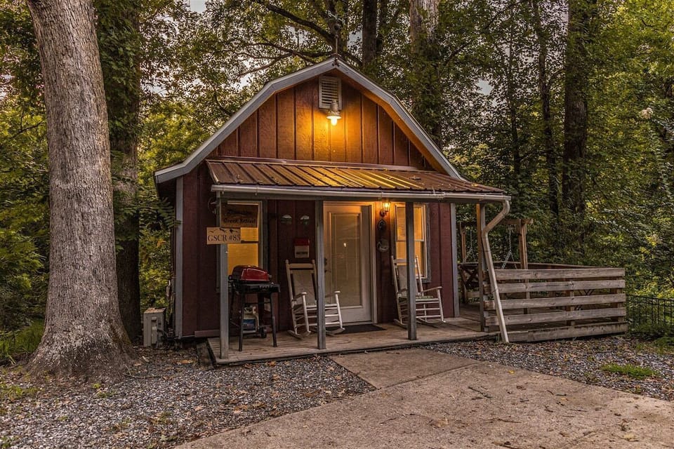 Front exterior illuminated by porch lighting with surrounding trees and private wooded setting. Inviting cabin atmosphere in the Smoky Mountains.
