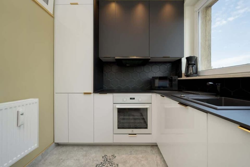 A compact, well-equipped kitchen with black countertops, under-cabinet lighting, and a clean, monochromatic palette.