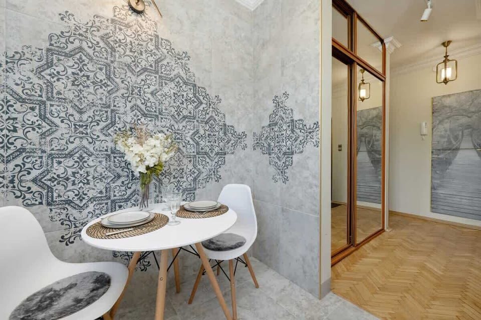 A charming breakfast nook with an intricate wall design, white chairs, and a vase of fresh flowers that brightens up the space.