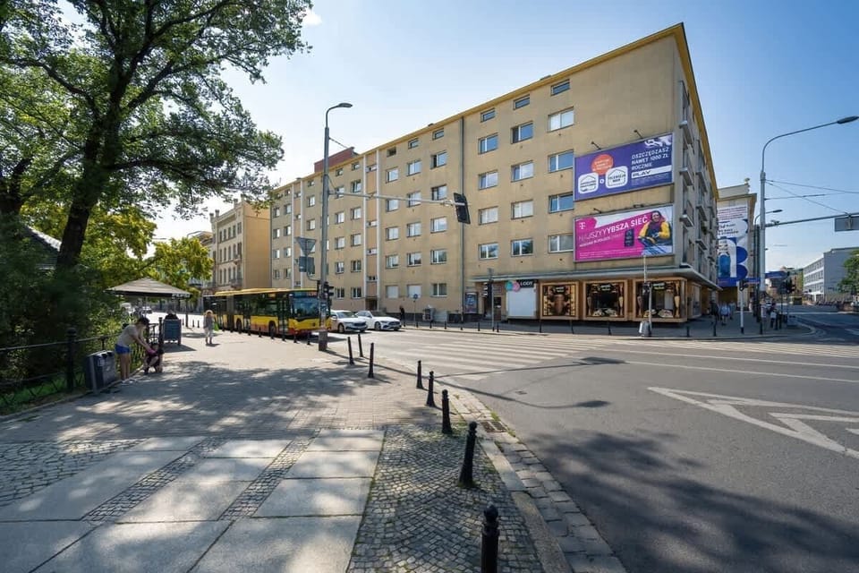 An outside view of the apartment block showing the street, parking area, and surrounding urban neighborhood.