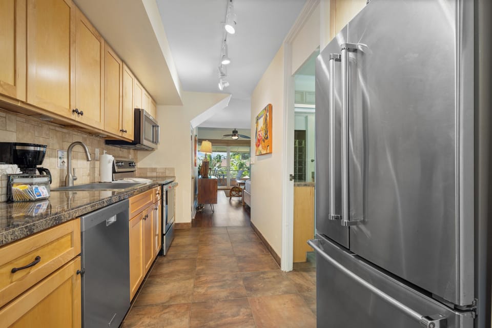 Your fully-equipped galley kitchen makes meal prep effortless with modern appliances, ample counter space, and warm natural light guiding you through to the inviting living area beyond.