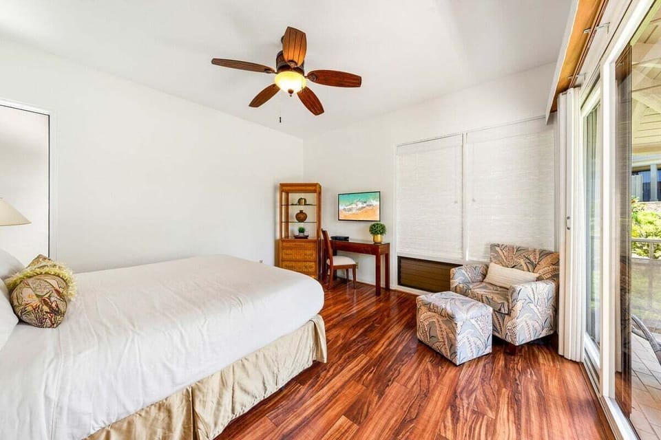 Inviting bedroom with a spacious layout, wood flooring, ceiling fan, nightstands, and soft natural light creating a relaxing island retreat.