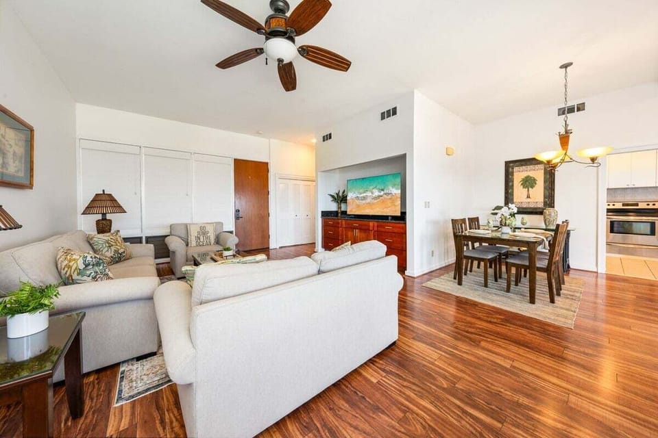 Stylish living room with hardwood floors, ceiling fan, modern furnishings, and an open layout connecting seamlessly to the kitchen and dining area.