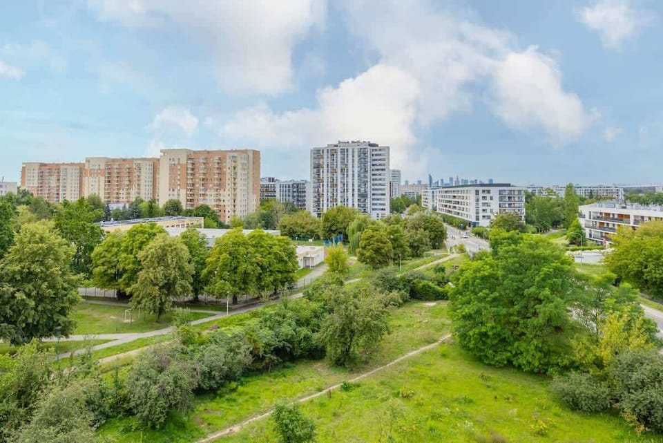 A lush green park area with manicured lawns and residential buildings in the background. Ideal for walking or relaxing in nature.