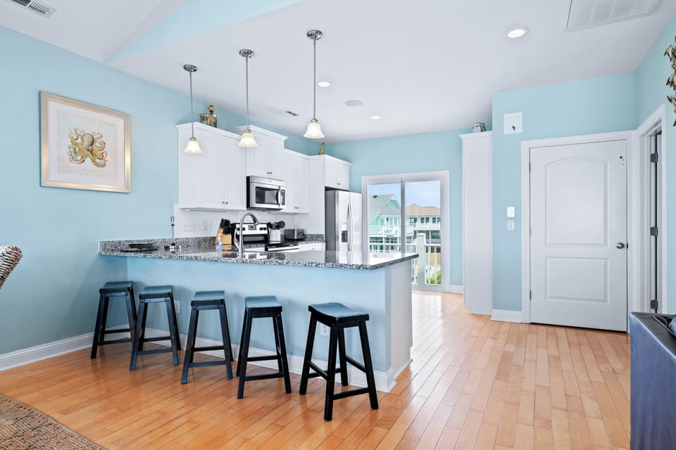 Relax at the breakfast bar while morning light streams through. The coastal-inspired kitchen features granite countertops, stainless appliances, and serene blue walls—your perfect retreat after beach days.