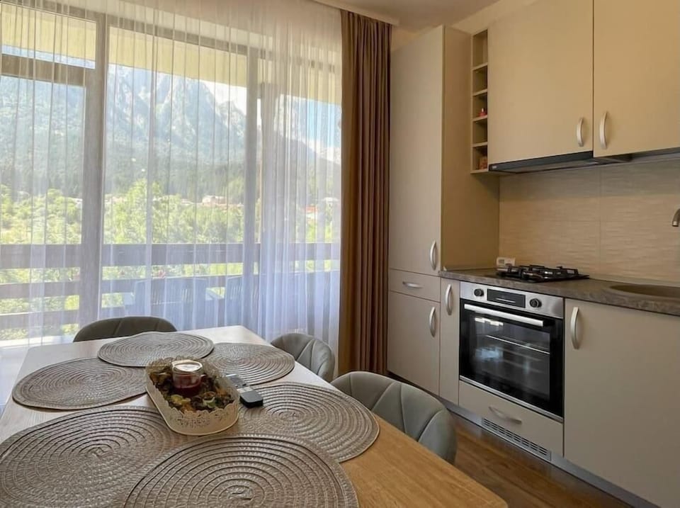 The modern open-space kitchen featuring a 2-burner stove, a dishwasher, toaster, Nespresso machine, coffee capsules, hood, refrigerator, TV, water kettle, dining table for 6 people, room-darkening shades and stunning mountain view from the balcony