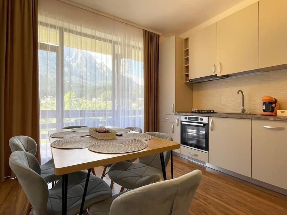 The modern open-space kitchen featuring a 2-burner stove, a dishwasher, toaster, Nespresso machine, coffee capsules, hood, water kettle, dining tables for 6 people, room-darkening shades and stunning mountain view from the balcony