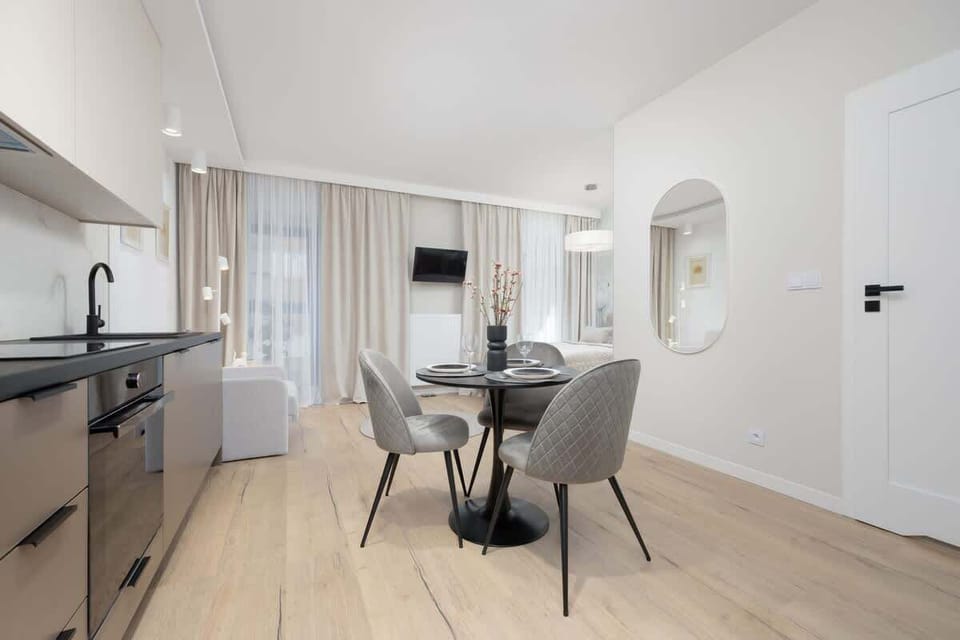A view of the dining and kitchen area, featuring a round table and grey upholstered chairs. The open layout maximizes space and function.