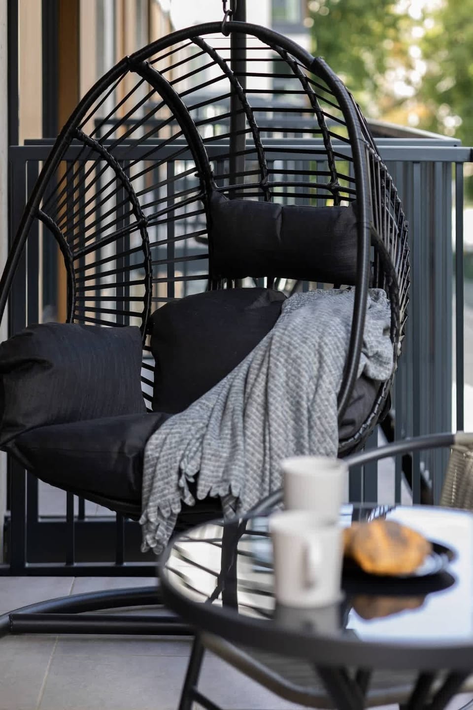A close-up of a hanging chair with a throw blanket and cup of coffee. A perfect nook for reading or relaxing on the balcony.
