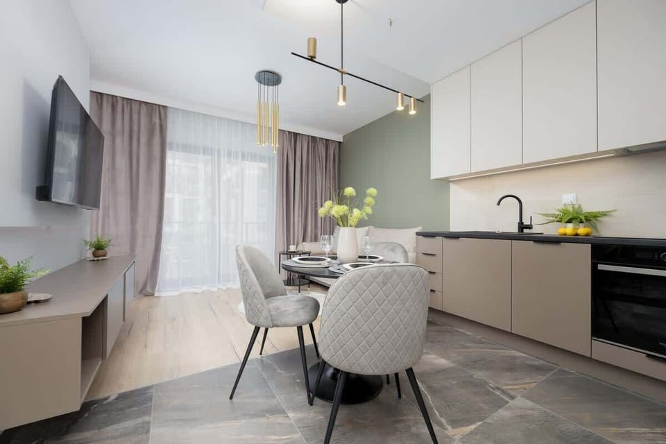 A modern kitchen with sleek cabinetry, a round dining table, and a wall-mounted TV. Light tones and minimalist design highlight the spacious layout.