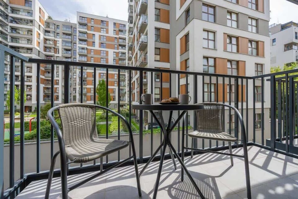 A balcony with a black metal table and chairs overlooking a modern residential complex. Perfect for enjoying a morning coffee outdoors.