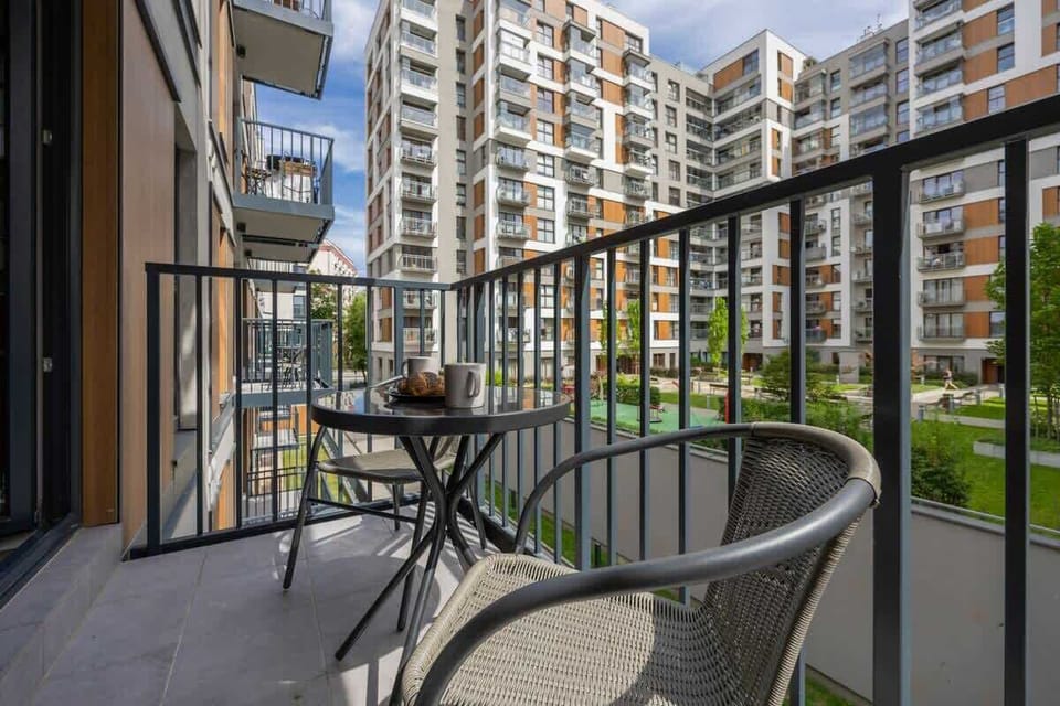 A balcony setup with a black table and chairs overlooking neighboring buildings. A cozy outdoor spot to relax in the fresh air.