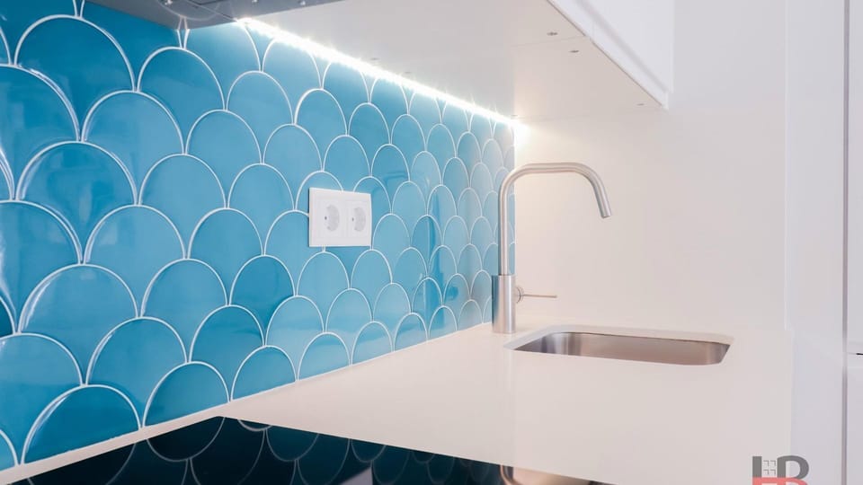 Prepare culinary delights in this vibrant kitchen, highlighted by a striking blue tiled backsplash and pristine white countertops, all illuminated by elegant under-cabinet lighting. This space offers a clean and inspiring environment for any meal prep.