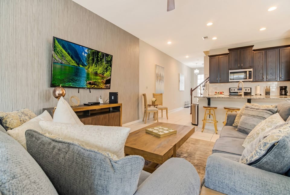 This bright, open living area offers a plush gray sofa and a stylish wooden coffee table, perfect for relaxation. The modern kitchen shines in the background, featuring sleek cabinetry and a warm ambiance from soft lighting.