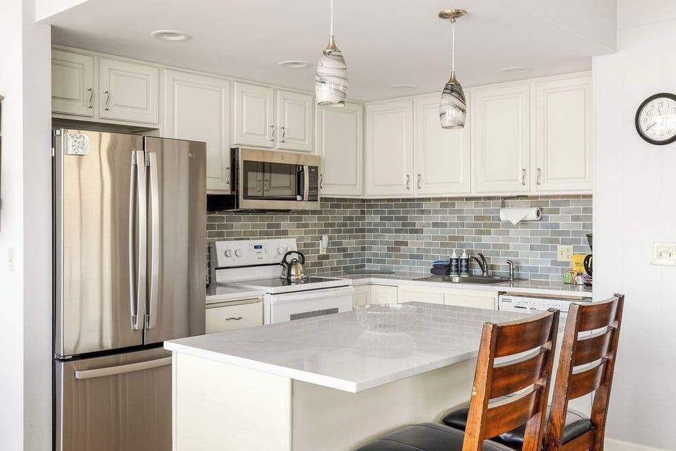 Spacious kitchen with stainless steel appliances, large island with seating, white cabinets, and subway tile backsplash.