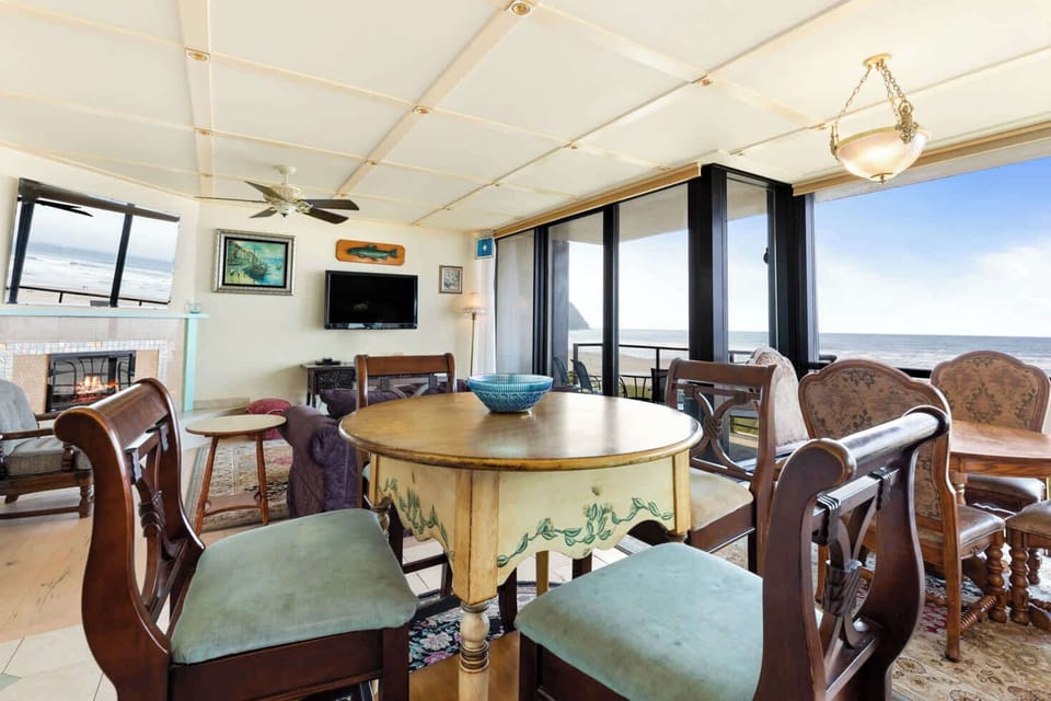 Breathtaking ocean views from your comfortable living and dining space! Features a modern fireplace, plush sofa, and an abundance of natural light showcasing the outdoor vista.