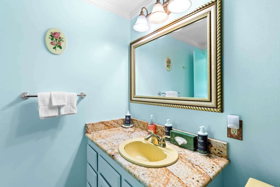 This colorful and functional bathroom offers a bright vanity, ample counter space, and a well-lit mirror for ultimate comfort and preparation.