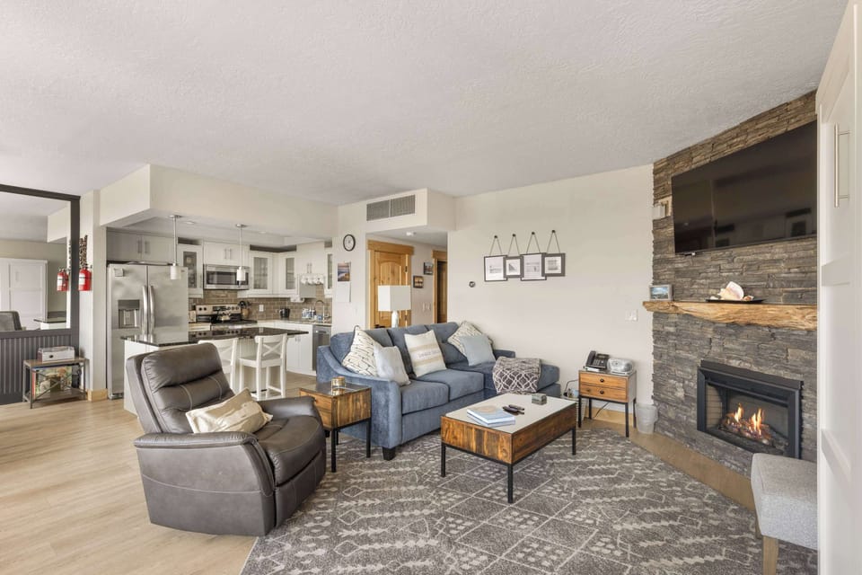 Warm and inviting living room featuring a cozy fireplace and plenty of seating, wrapped by large windows allowing natural light to enter.