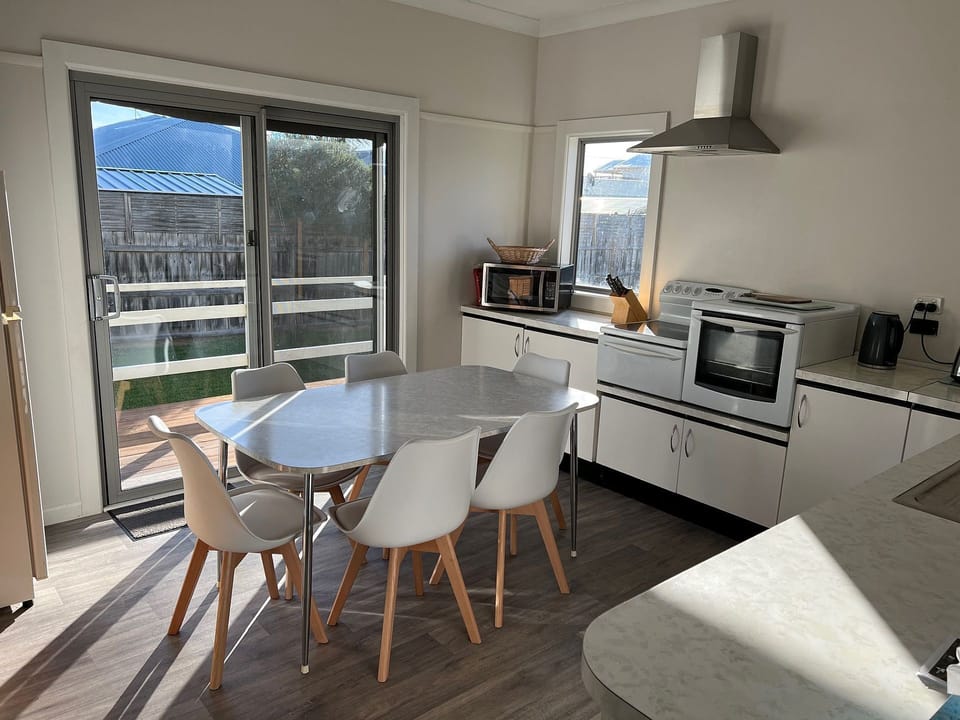 Dining table with 6 chairs, microwave, electric stove with oven, kettle, toaster, pod coffee machine, dishwasher, fridge with freezer, sliding door exiting to the side deck.