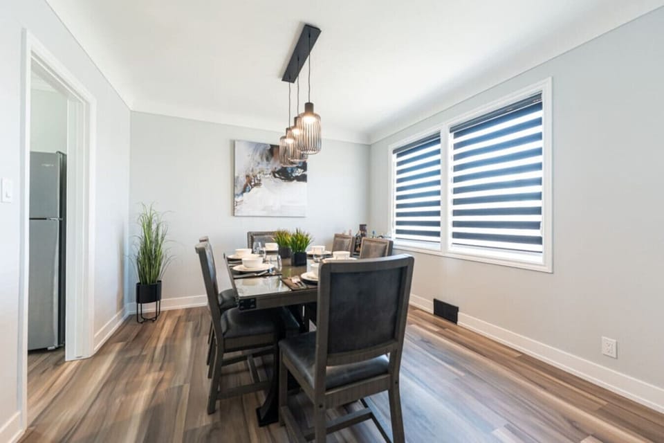 `Dine in elegance! Our spacious dining area features a large table set for six, complemented by comfortable chairs. Modern pendant lights illuminate contemporary wall art, creating a sophisticated ambiance.