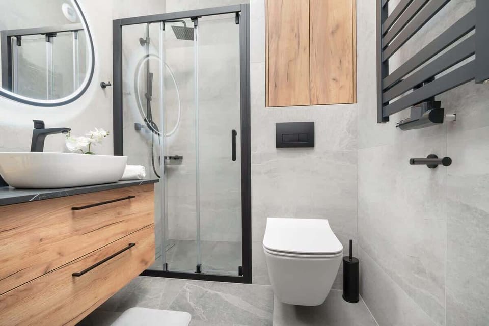 A compact bathroom with a modern sink, toilet, and wooden storage cabinets. Grey and white tones create a fresh feel.