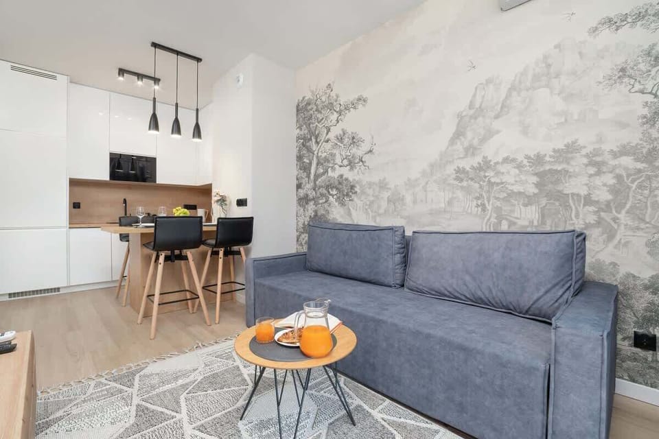 A similar living room angle showing the grey sofa and coffee table. The background reveals the kitchen area for a connected home feel.