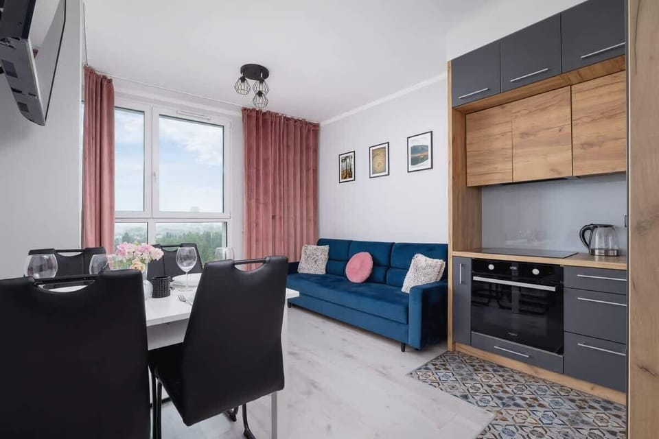 Combined living and dining area with a kitchen; black chairs, wooden cabinetry, and a round dining table.