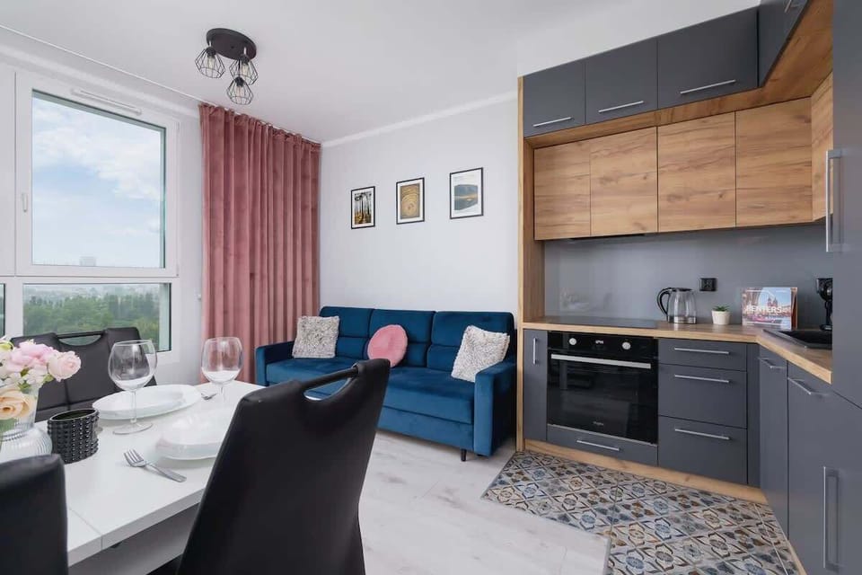 Combined living and dining area with a kitchen; black chairs, wooden cabinetry, and a round dining table.