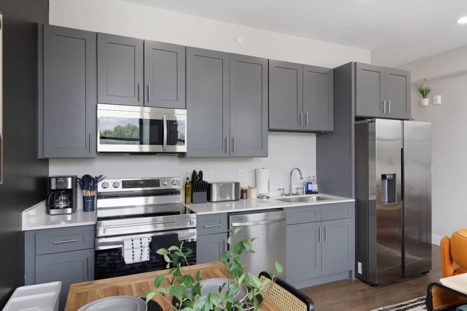 This modern kitchen features a spacious island with cabinetry, sleek white countertops, stainless steel appliances, open shelving, and stylish lighting.